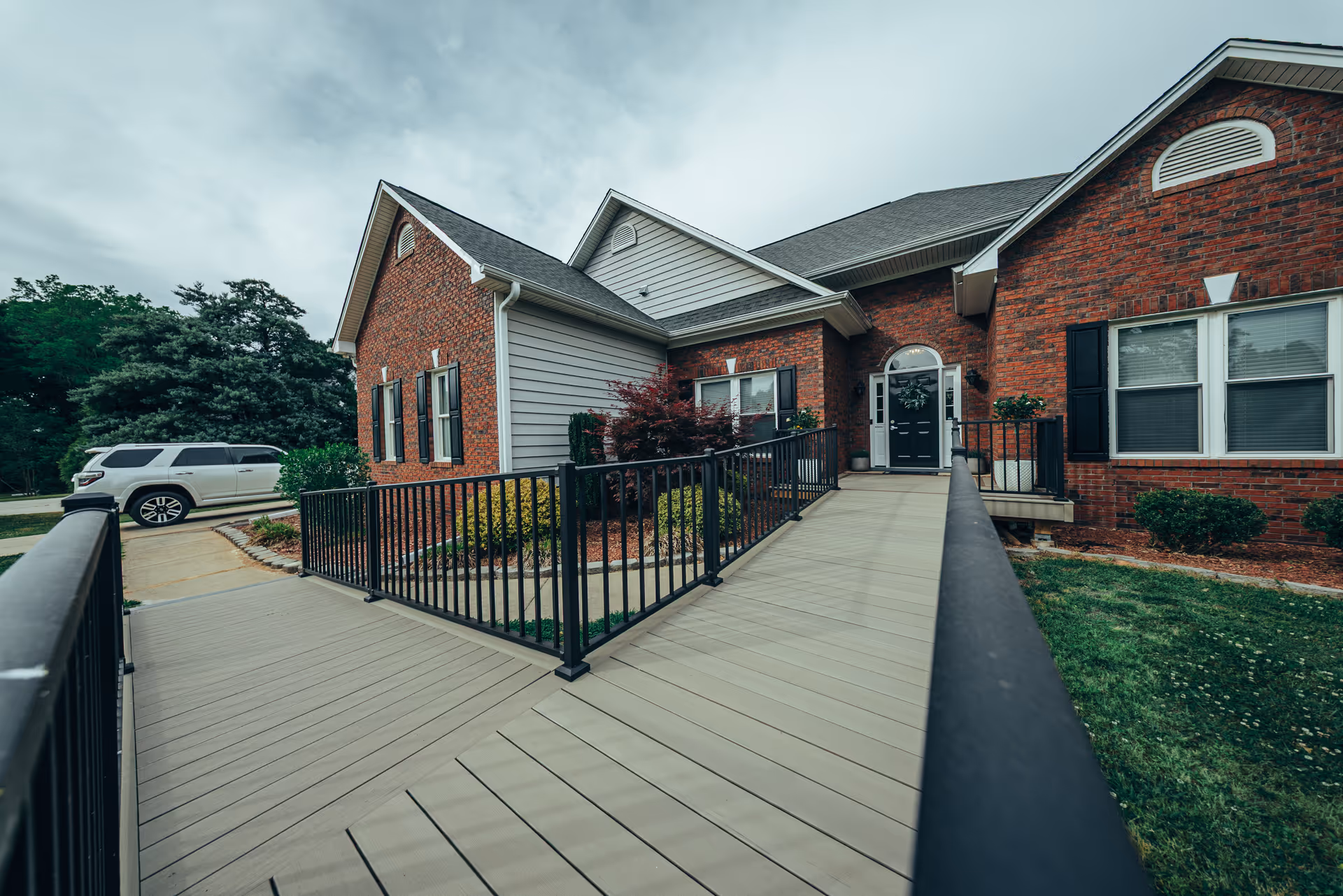 Brick senior care home exterior with ramped entrance, black railing, and large windows.