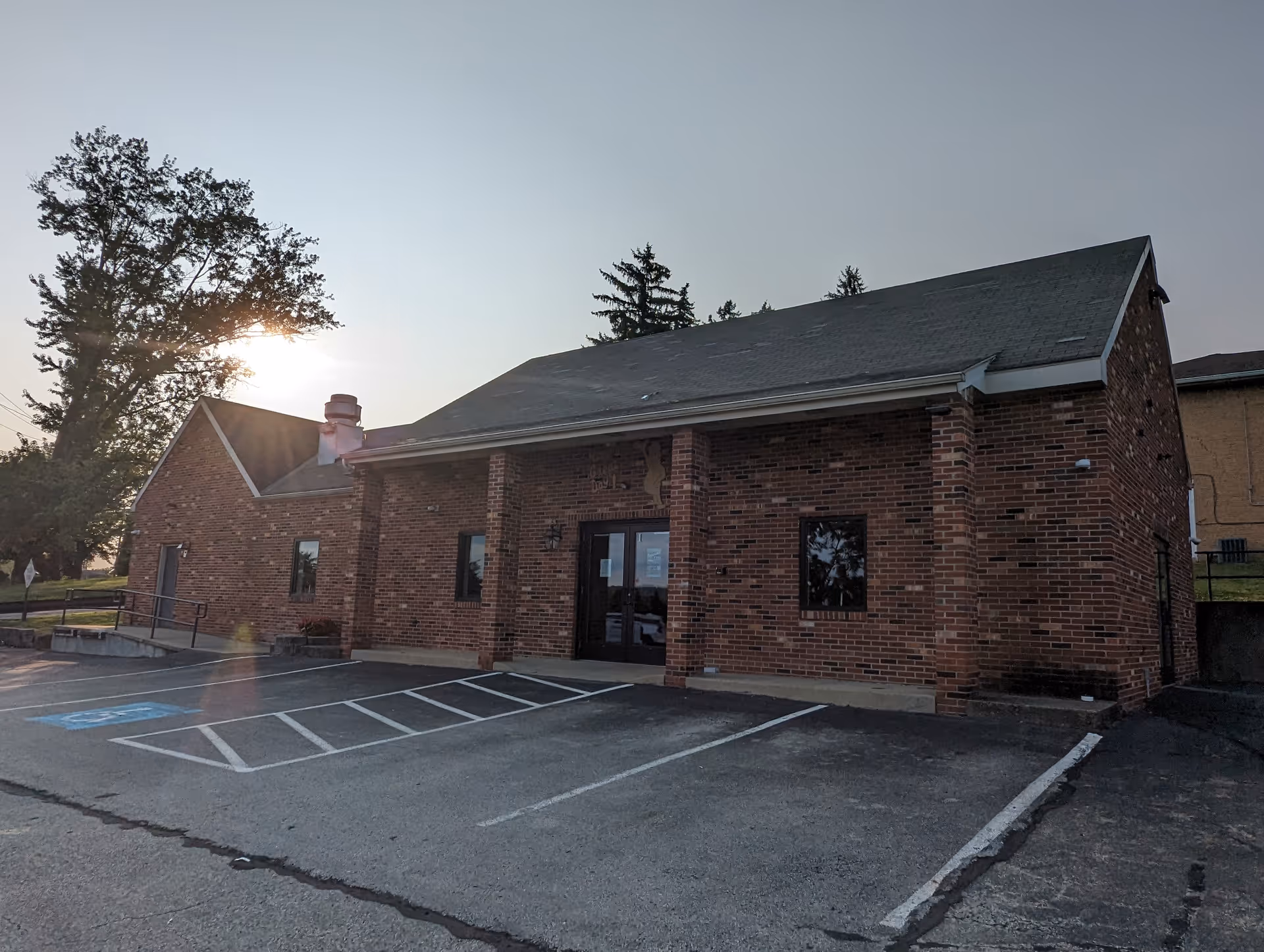 Brick facility with a gabled roof, glass entrance, and lined parking lot.