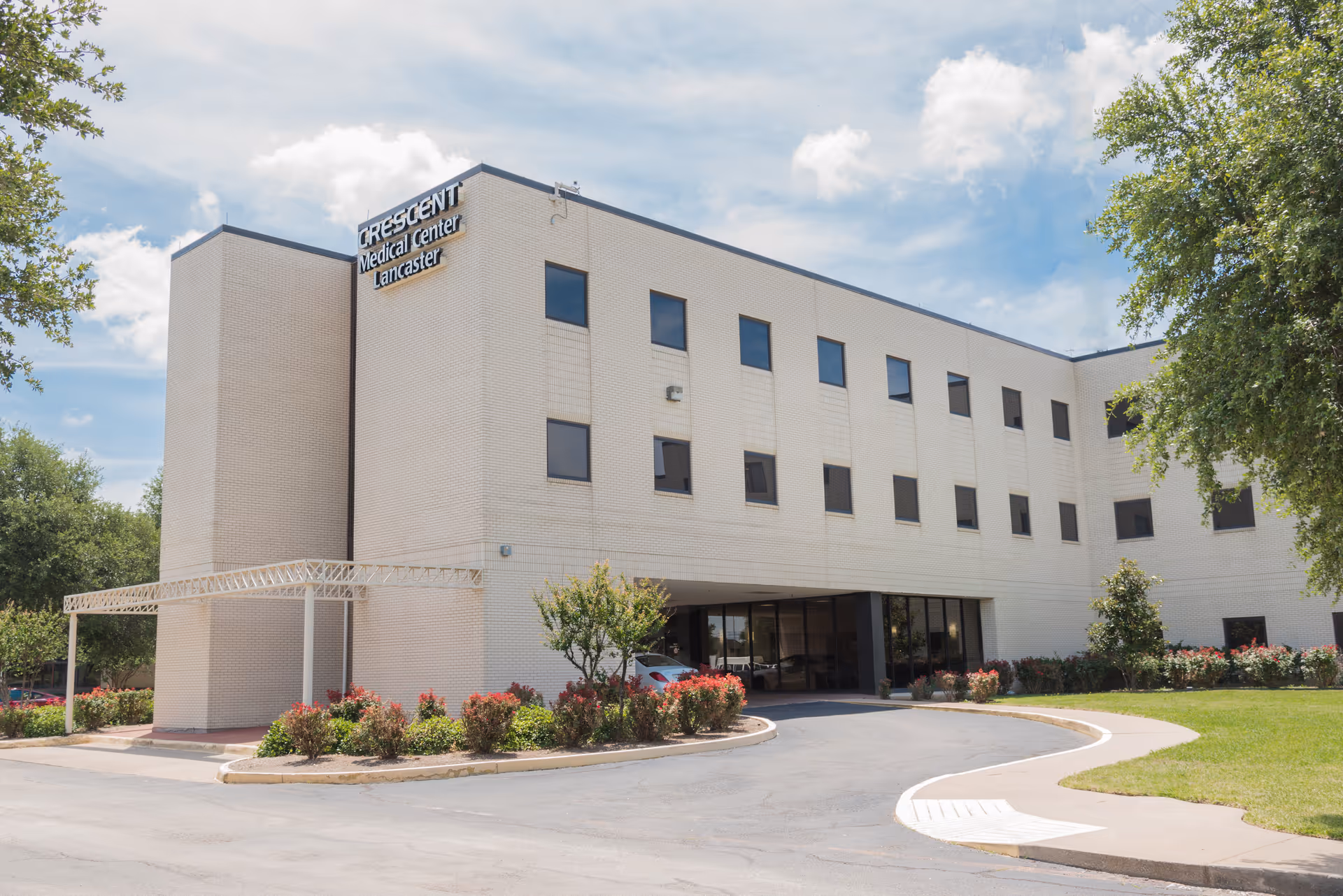 Light-colored, multi-story hospital building with curved driveway and landscaped entry.