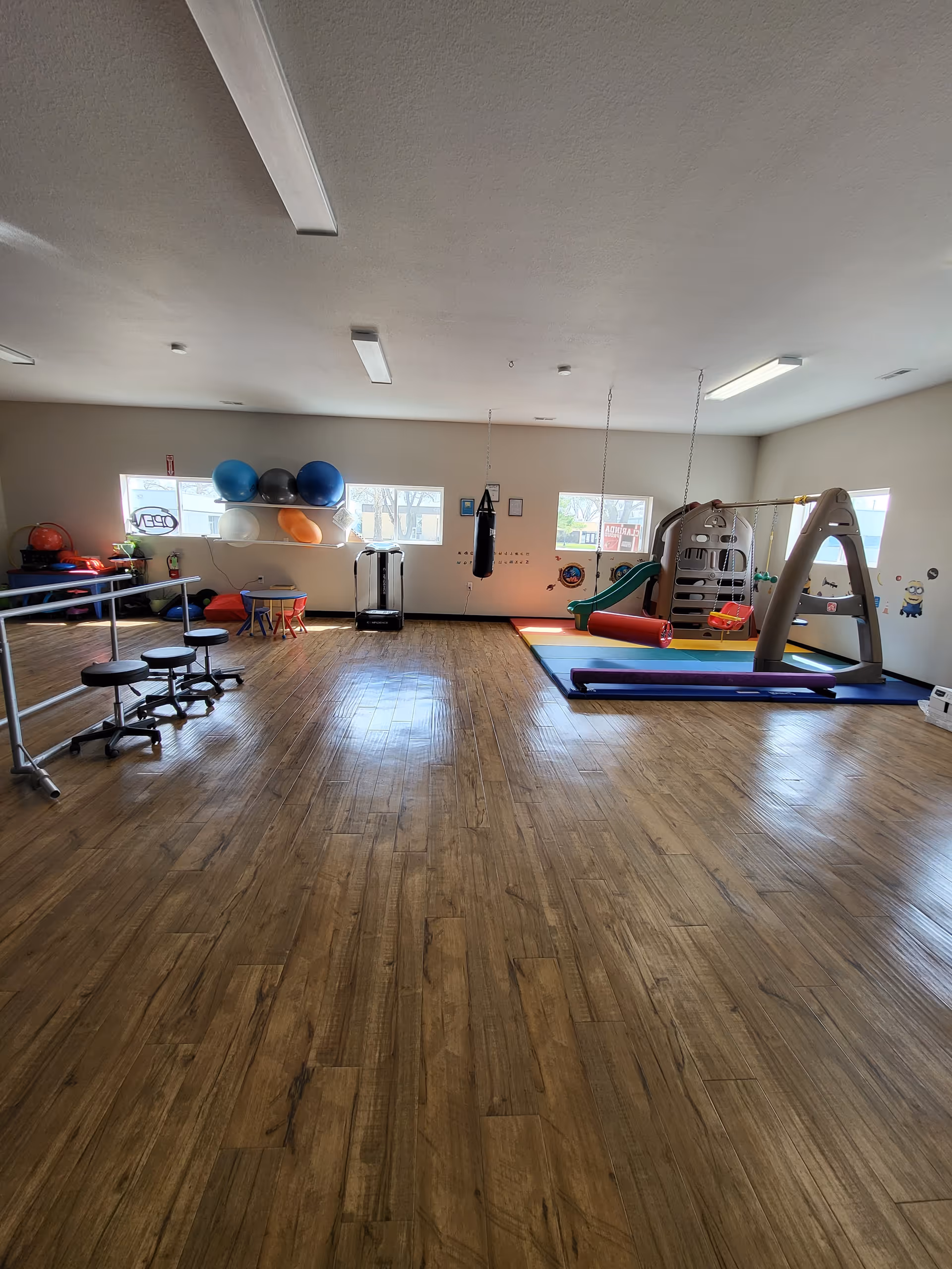 Spacious indoor activity room in a senior facility with gym equipment and a play structure.
