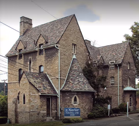Stone multi-story historic building with steep pitched roofs and a sign reading 'Xavier Personal Care Home' at the front.