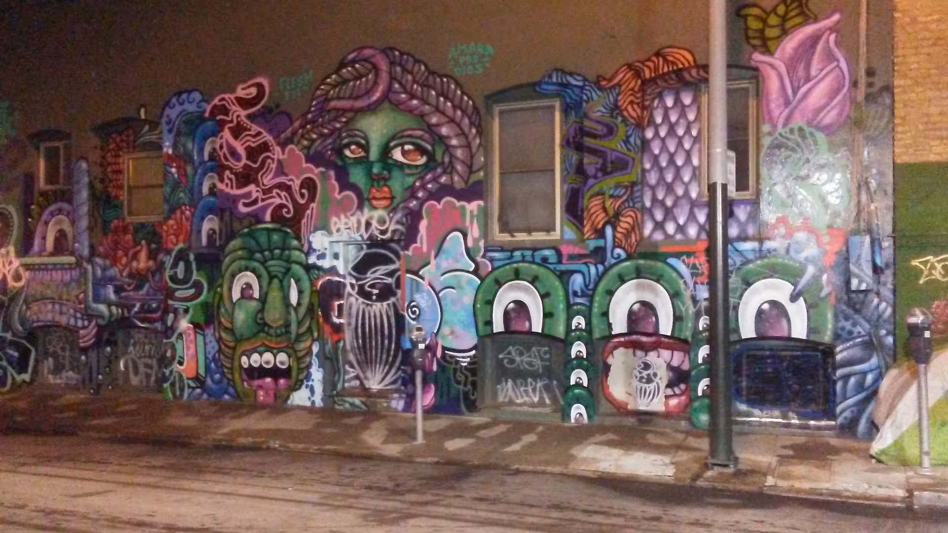 Exterior wall covered in colorful graffiti murals beside a sidewalk and street.