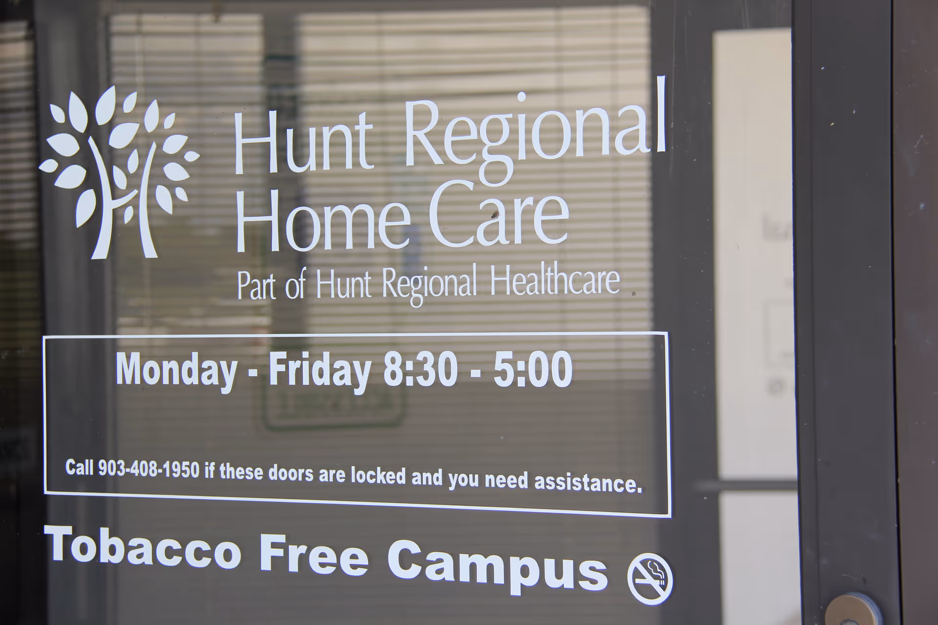 Glass door displaying Hunt Regional Home Care signage, hours, and tobacco-free campus notice.