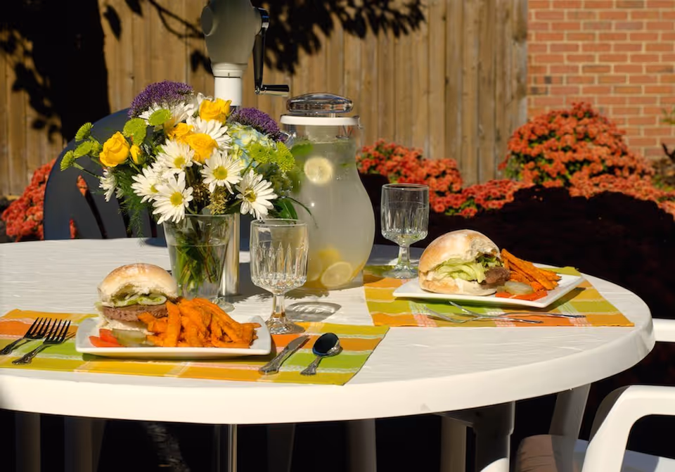 Outdoor dining table with burgers, fries, lemonade, and a flower centerpiece.