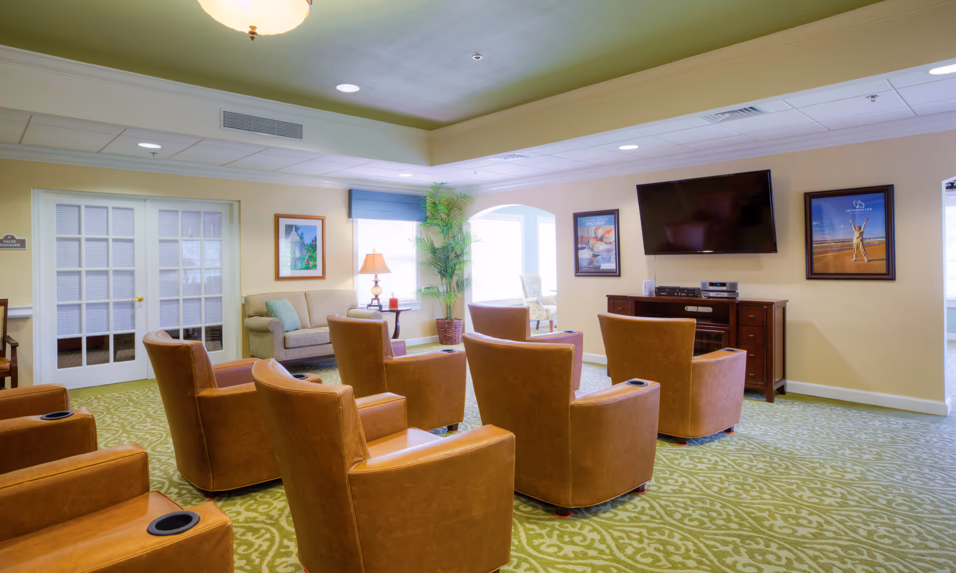 Cozy adult living room lounge with brown leather chairs, carpet, and a wall-mounted TV.