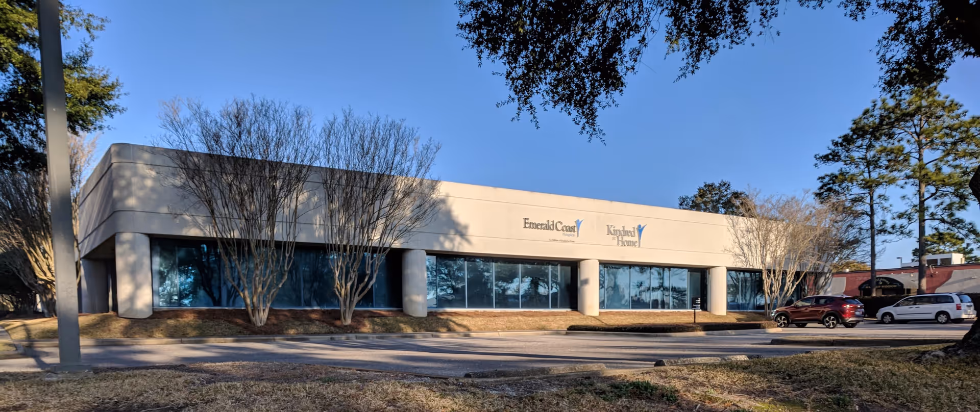 Exterior of Emerald Coast Hospice facility with large glass windows and parking lot
