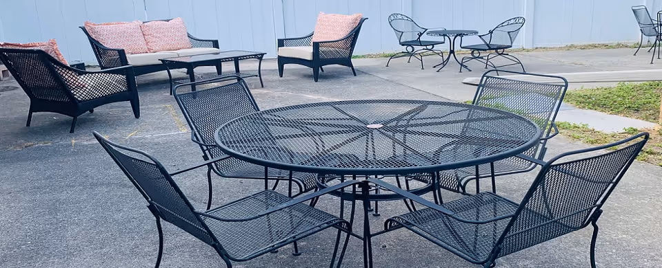 Outdoor patio with metal tables and chairs, cushions against a pale blue wall.