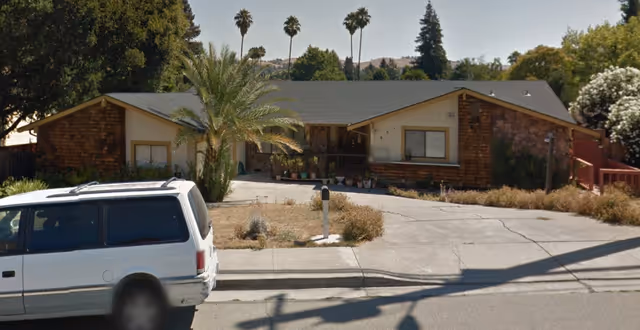 Front view of a single-story senior living home with a driveway and a parked white van.