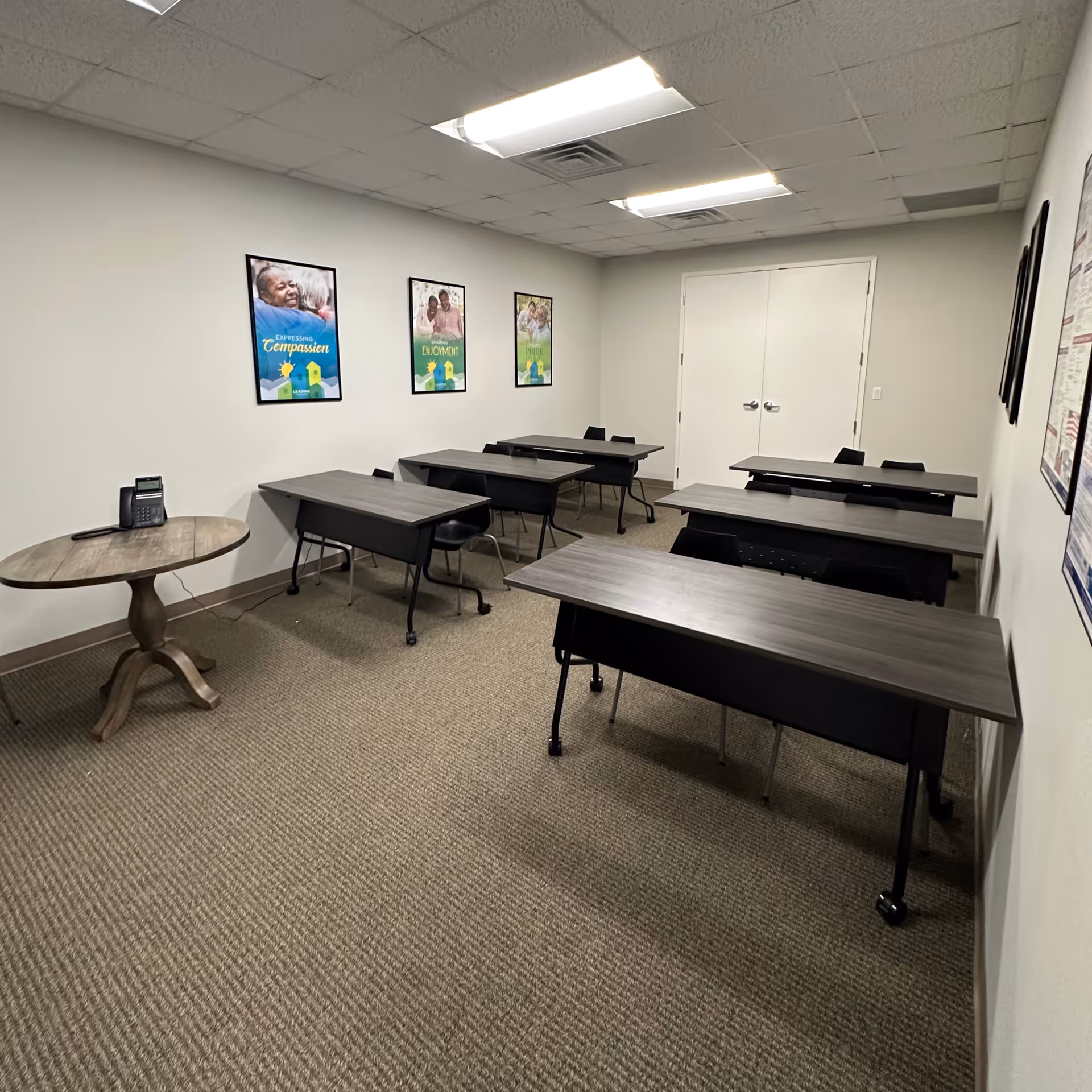 Interior classroom setup with desks, chairs, posters, and a round table in a senior facility.