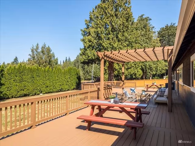 Sunlit wooden outdoor deck at a senior living facility with seating and a pergola.