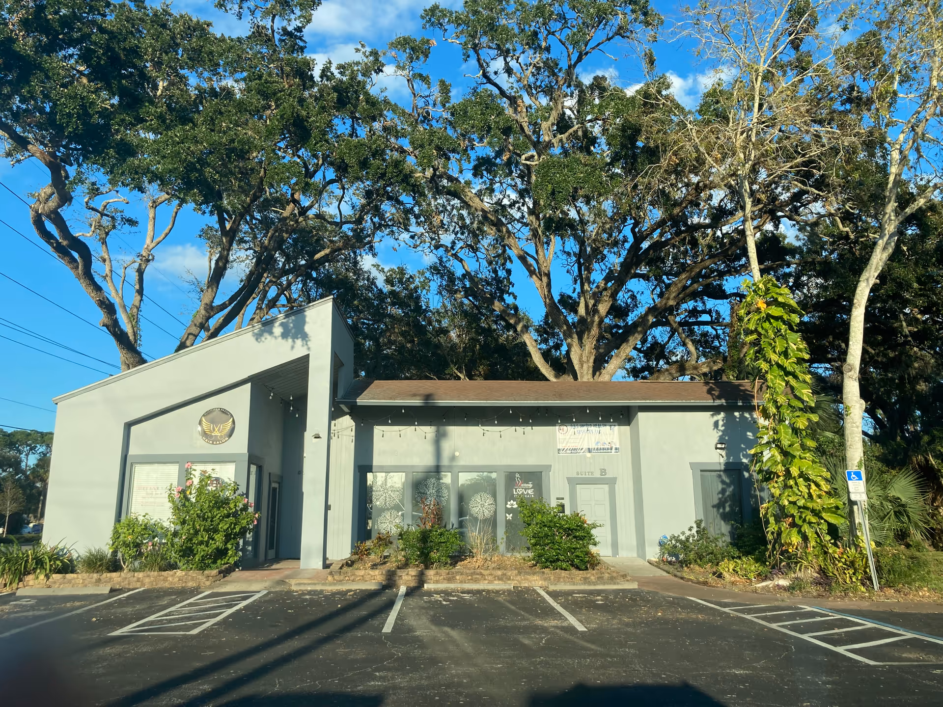 Exterior view of a single-story medical facility with a small parking lot and large trees.