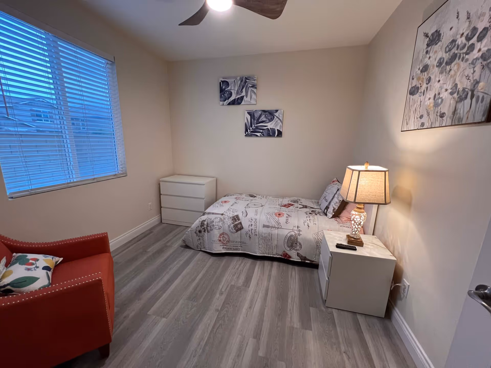 Small Bliss Homes bedroom with bed, dresser, nightstand, lamp, chair, and wall art.