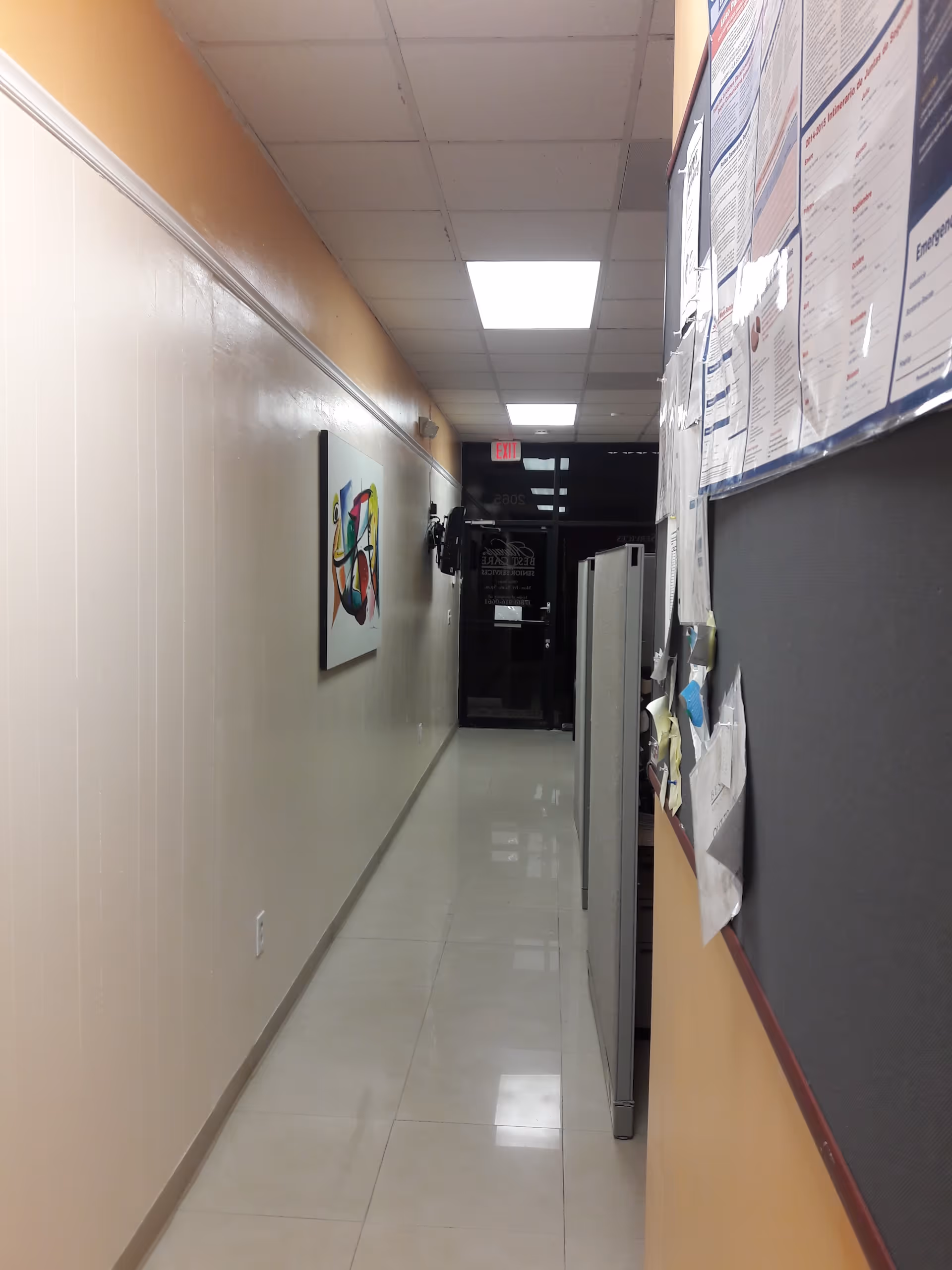 Narrow hallway inside a senior care facility with bulletin boards and ceiling lights.