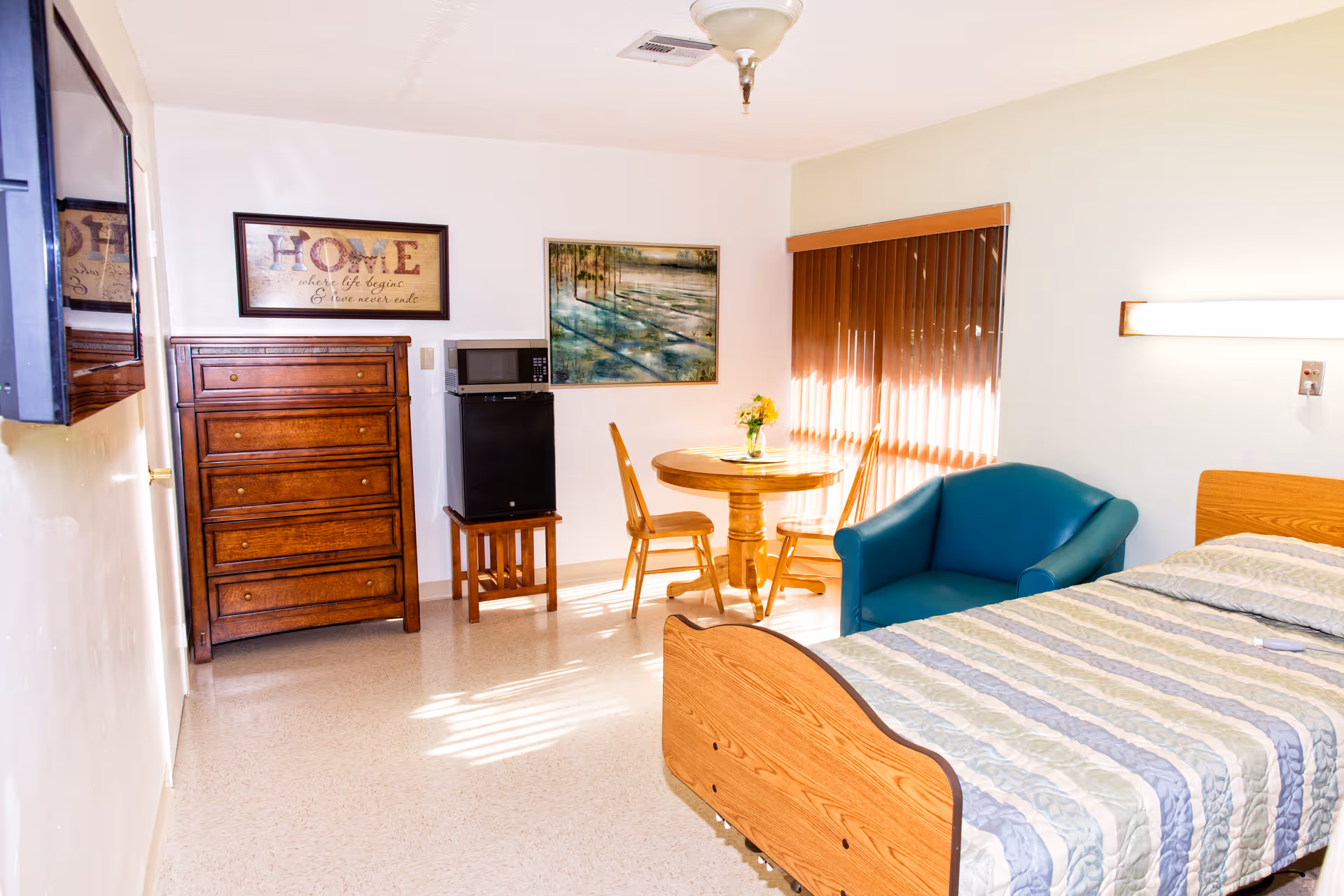 A furnished bedroom with a bed, dresser, round table, chairs, and a blue sofa.