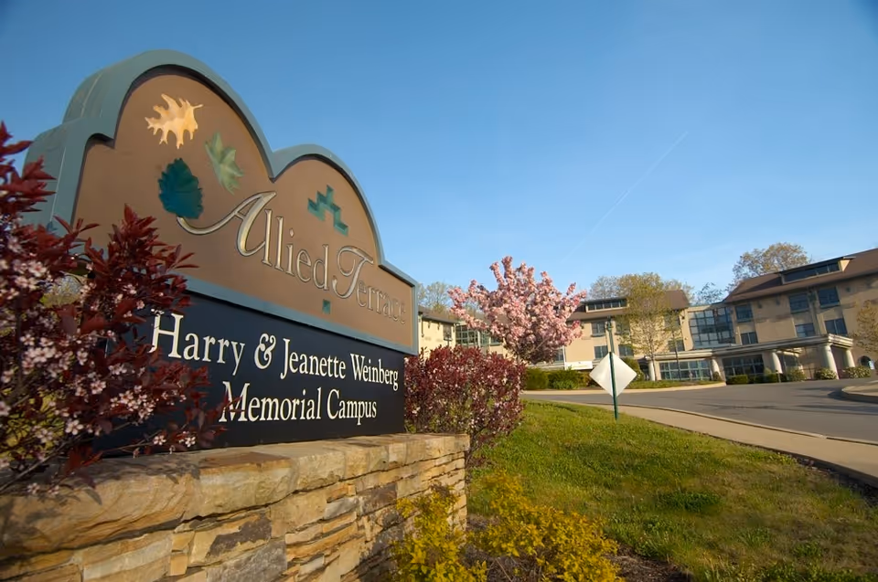 Exterior view of Allied Terrace sign with campus buildings and blooming trees.