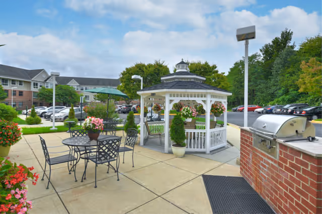 Outdoor patio area with a gazebo, metal tables, chairs, potted flowers, and grill.