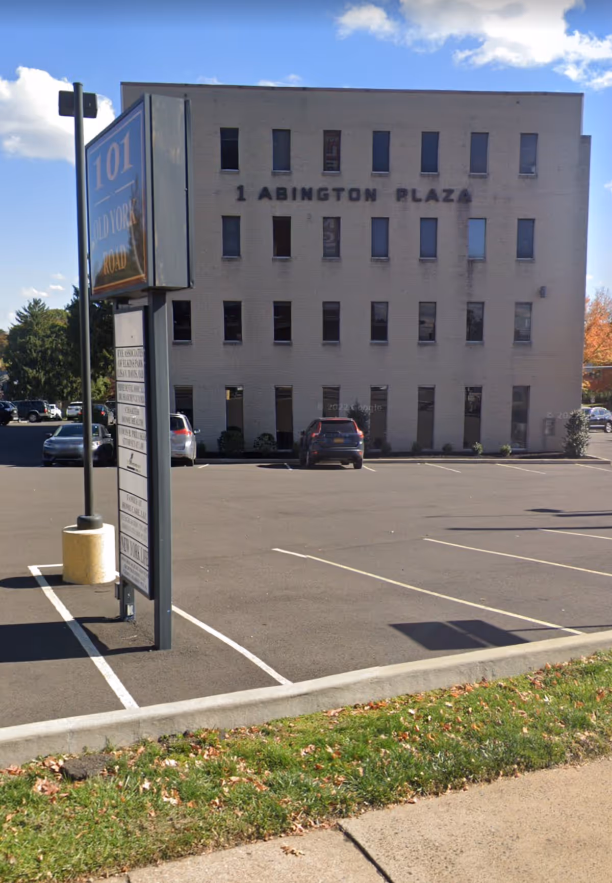 Exterior view of a light-colored three-story building labeled Abington Plaza with a parking lot.