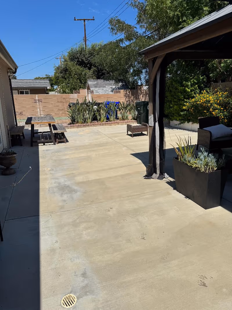 Sunlit outdoor patio with tables, seating, and planters at a senior facility.
