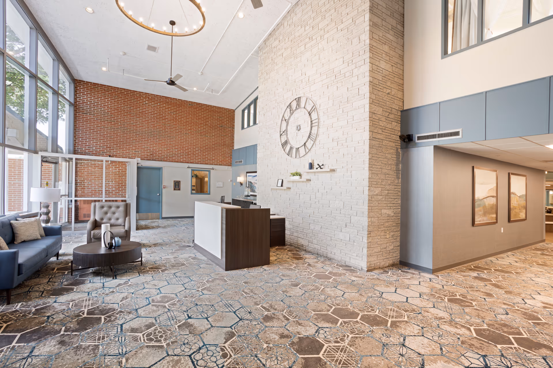 Spacious modern lobby with reception desk, seating area, brick wall, and a large clock.