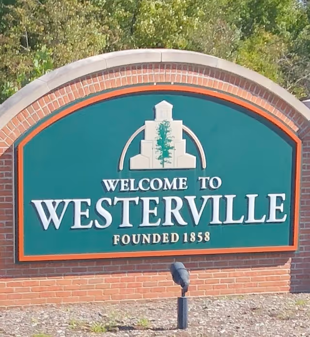 A brick-arched sign that says 'Welcome to Westerville' with a green background and surrounding greenery.