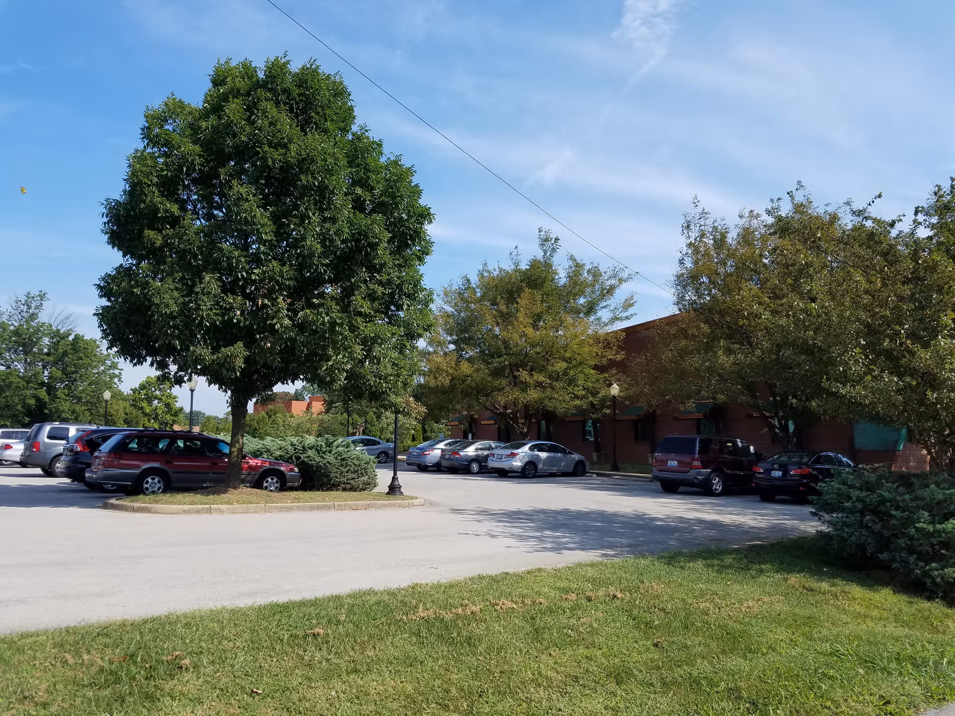 A parking lot in front of a brick building with trees and clear blue sky.