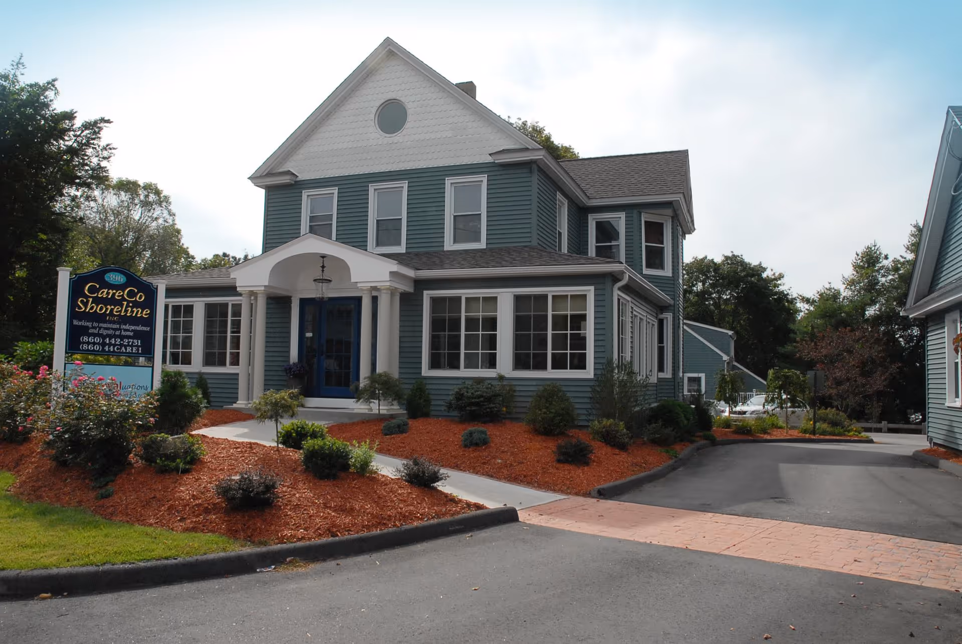 Blue two-story senior living building with landscaped front yard and sign