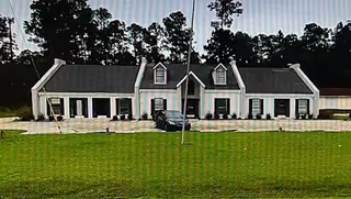 Exterior view of a long, light-colored senior care facility with gabled roofs and a grassy foreground.
