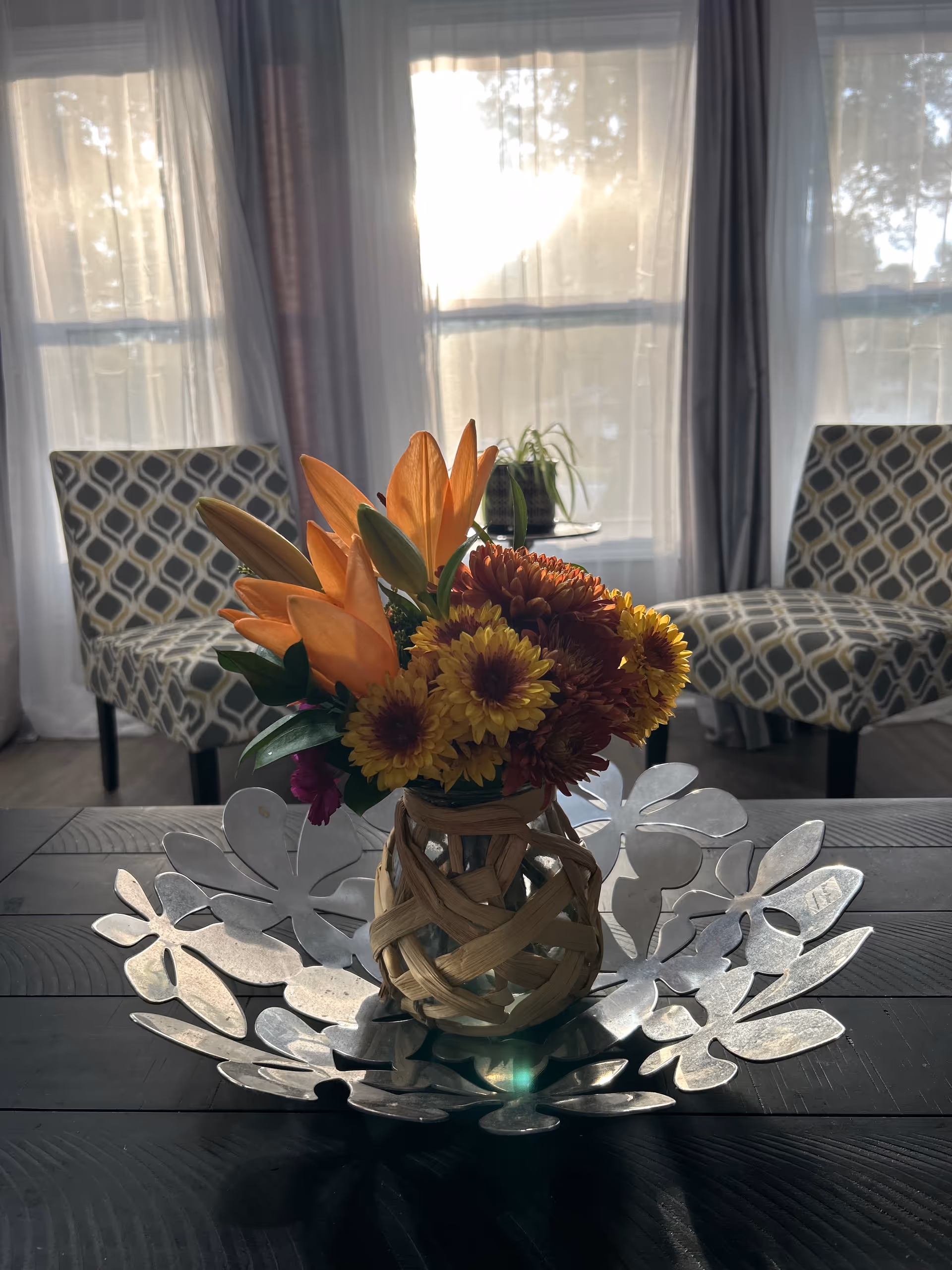 Flower centerpiece on a dark table in a sunlit lounge with patterned chairs