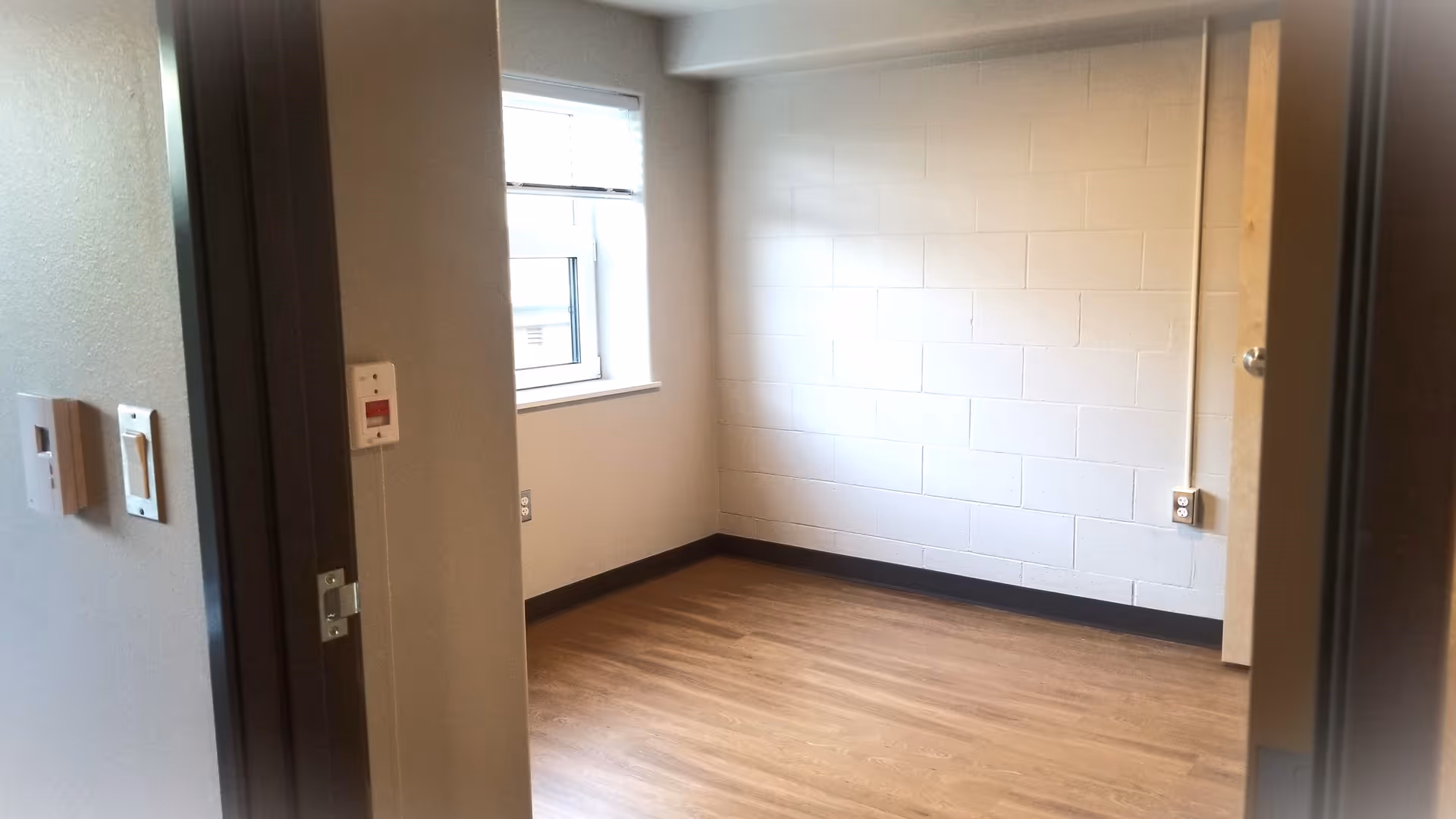 Empty room with wood-look flooring, a white cinderblock wall, and a window.