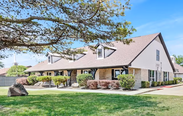 A single-story building with a gabled roof, stone accents, and manicured shrubs.
