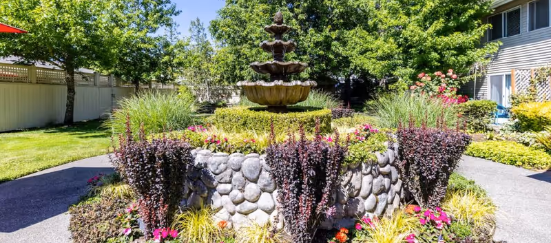 Sunny courtyard fountain surrounded by colorful garden beds at Aegis Living Lynnwood.