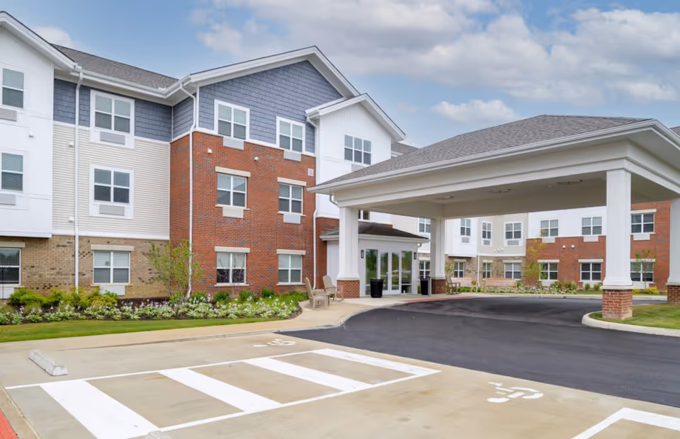 Exterior view of a senior living facility with brick and white siding and a covered entrance.