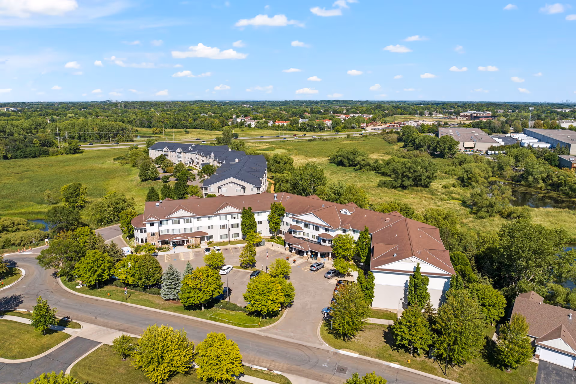 Aerial view of Cornerstone Assisted Living and Memory Care campus with brown-roofed buildings, parking, and trees.