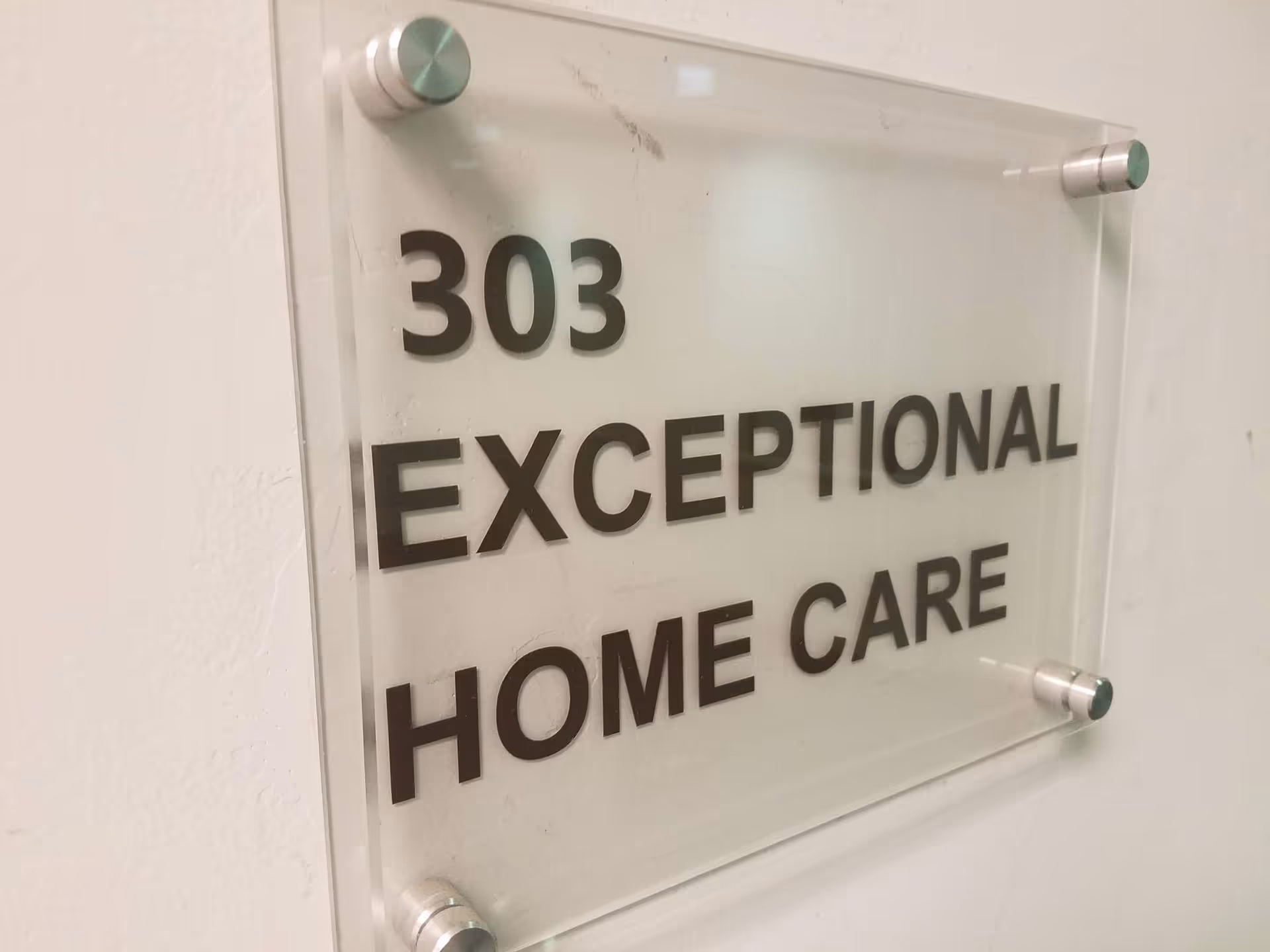Acrylic wall plaque displays room number 303 and text Exceptional Home Care in a hallway.