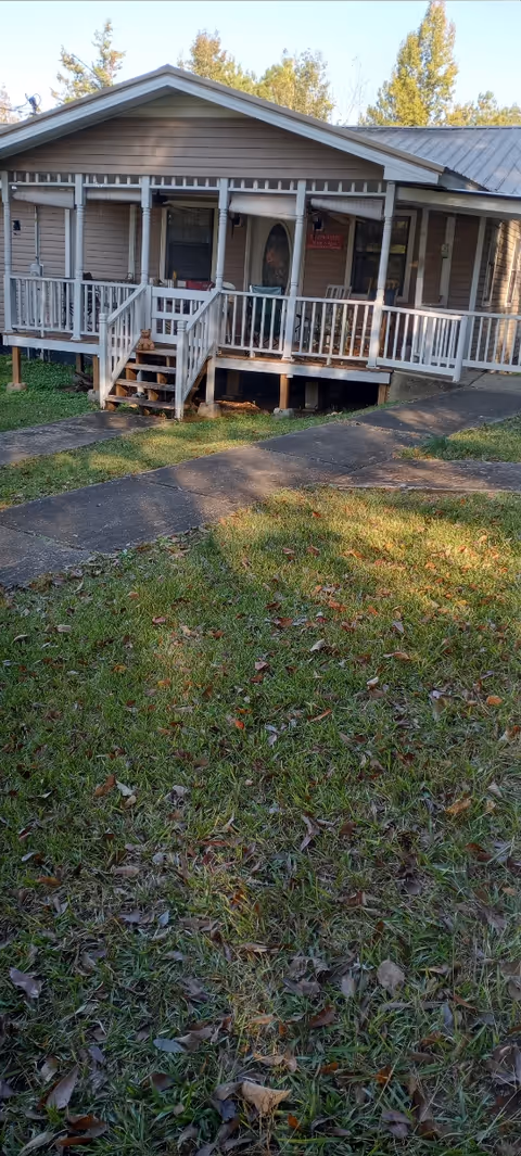 A single-story brown building with a wraparound white porch and front steps.