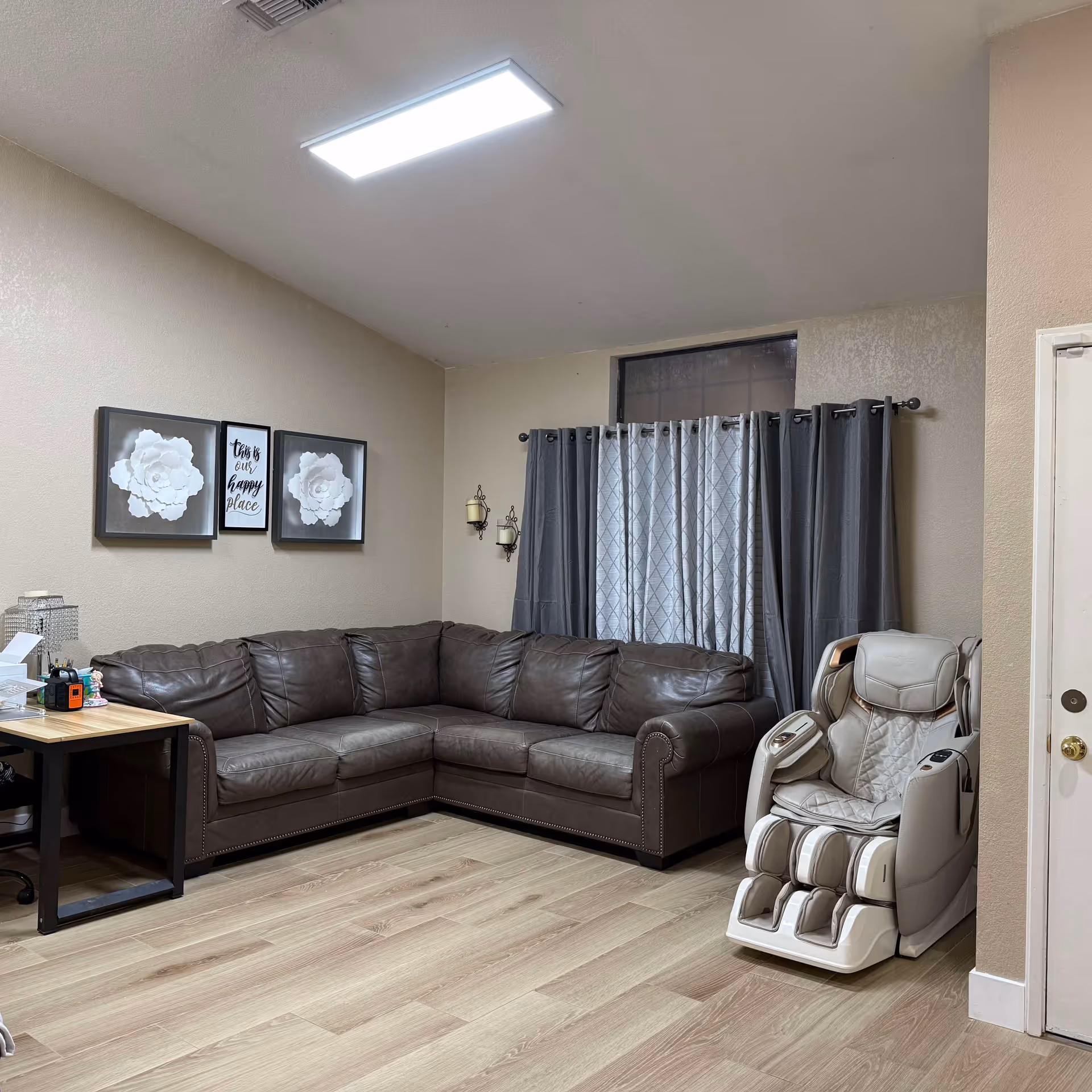 Cozy living room with dark sectional sofa, massage chair, desk, and wall art.