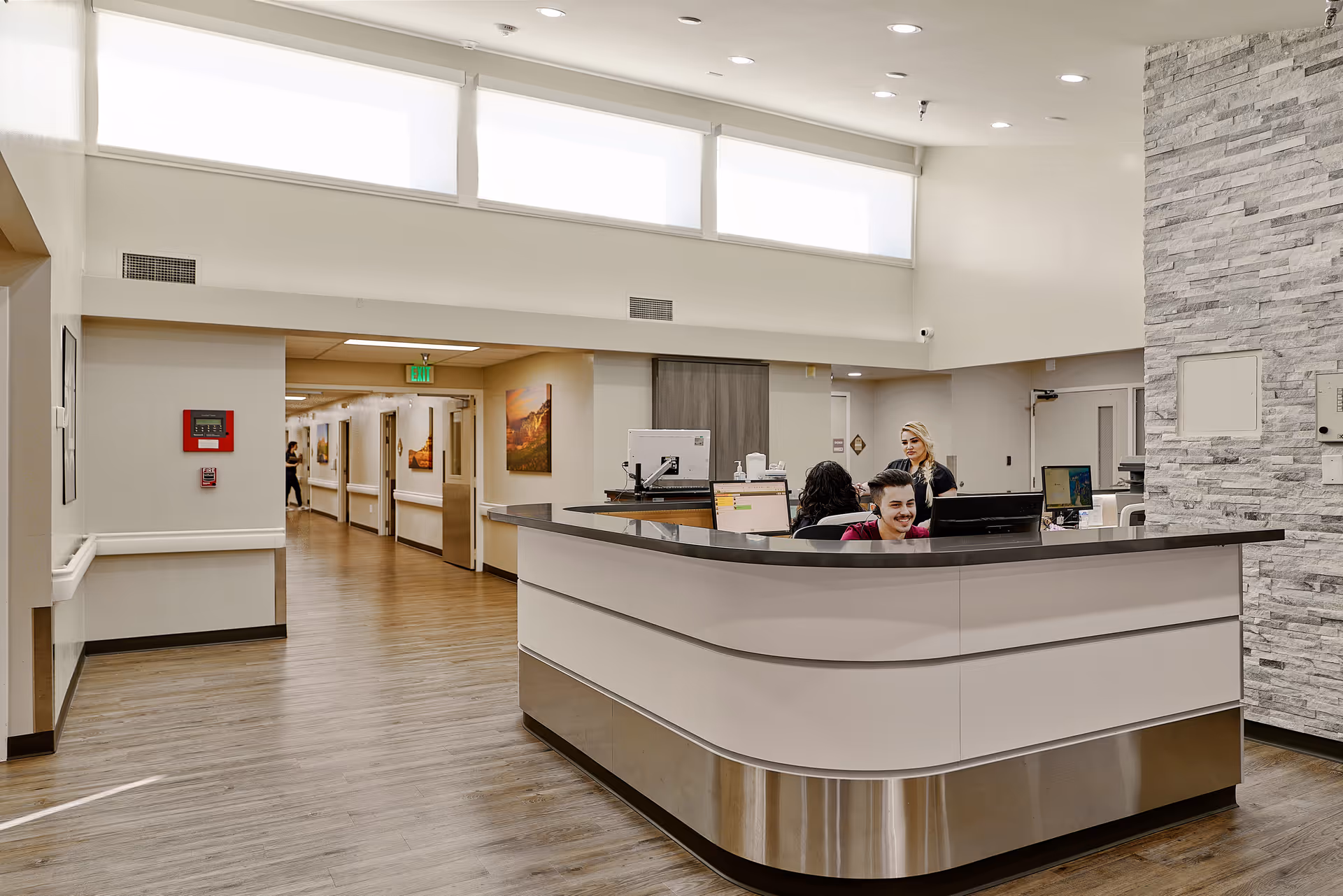Bright lobby with a curved reception desk, stone wall, and staff at computers.
