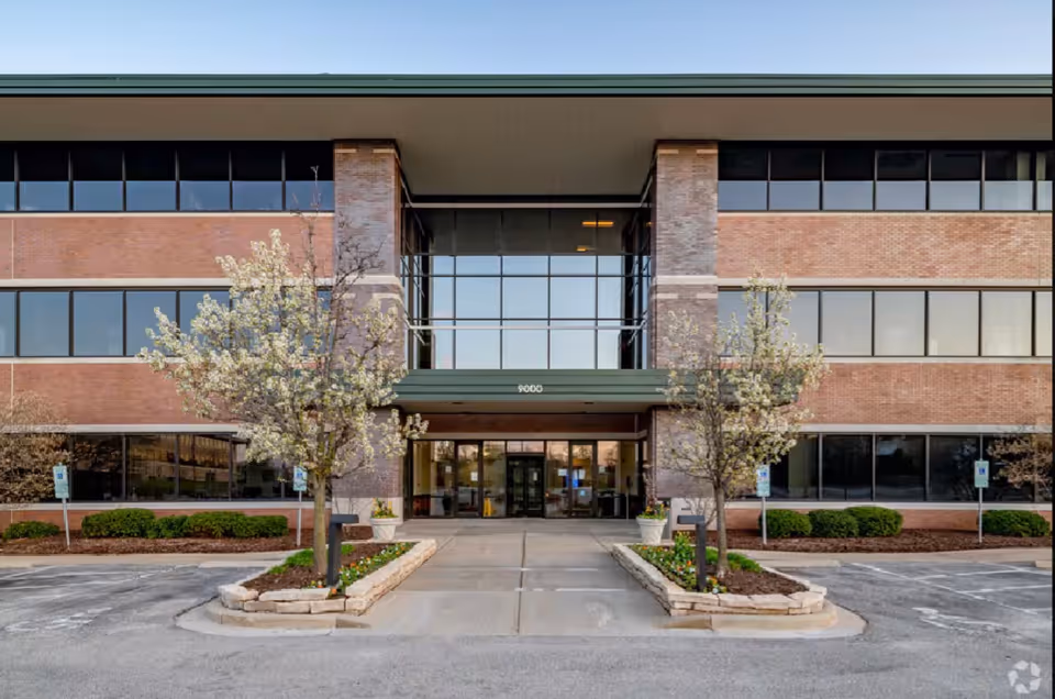 Exterior view of a senior living facility building front with brick facade and glass entrance.