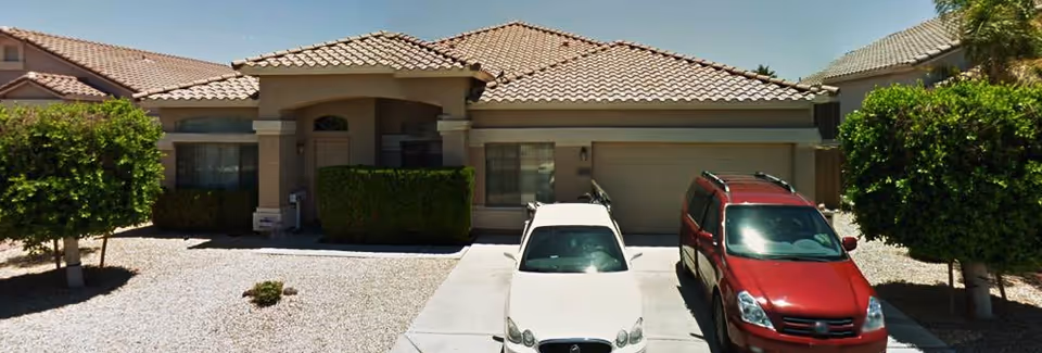 Single-story beige house with tile roof and two cars parked in the driveway.