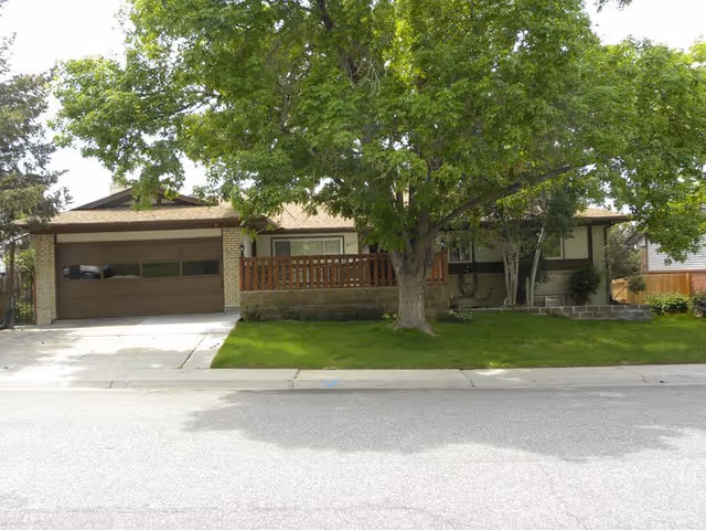 Front view of a single-story senior living home with a garage, porch, and large tree.