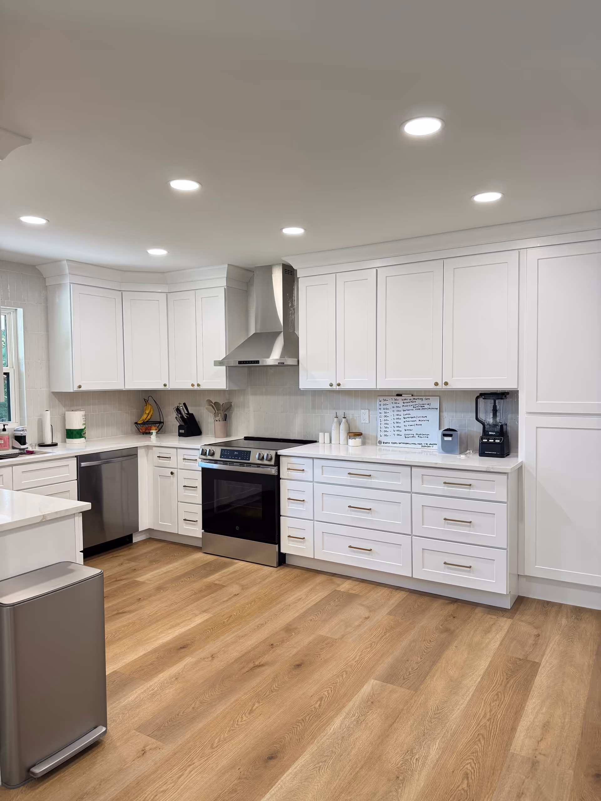 Bright white kitchen with stainless appliances and light wood flooring.
