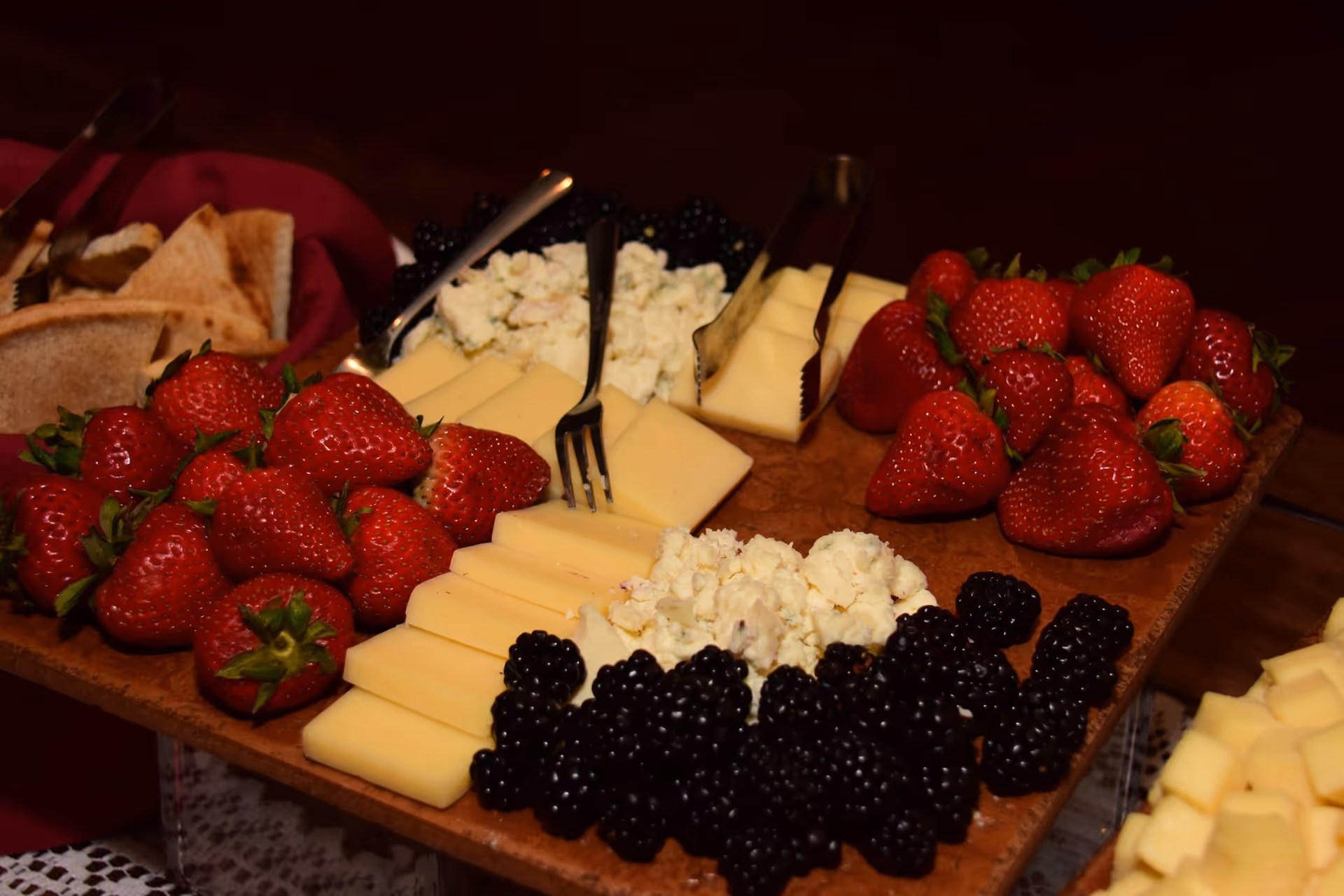 Assorted cheeses, fresh strawberries, blackberries, and bread on a wooden serving board.