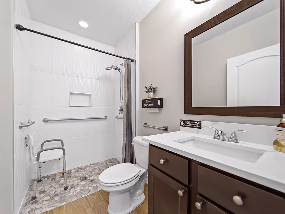 Accessible bathroom with walk-in shower, grab bars, a shower chair, sink, and mirror.