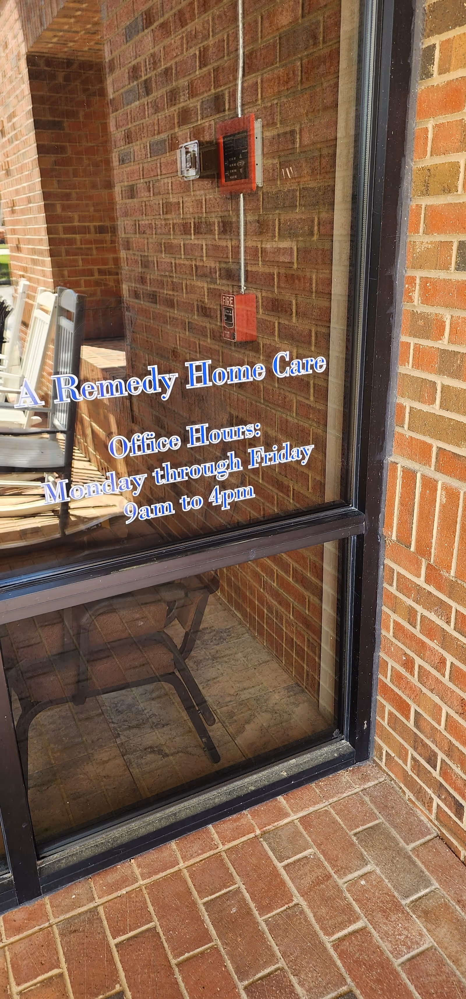 Glass door with brick exterior shows A Remedy Home Care sign and office hours.