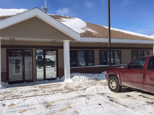 Front exterior of a Pro-Health Care facility with snow, glass doors, and a red pickup.