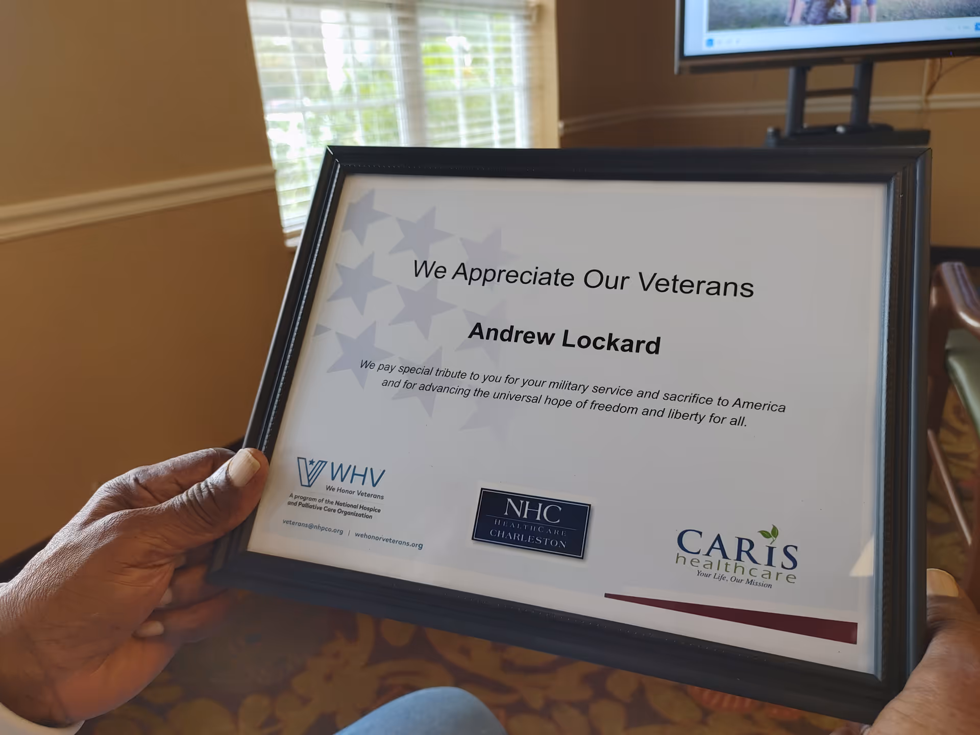 Framed certificate reading 'We Appreciate Our Veterans' held indoors.