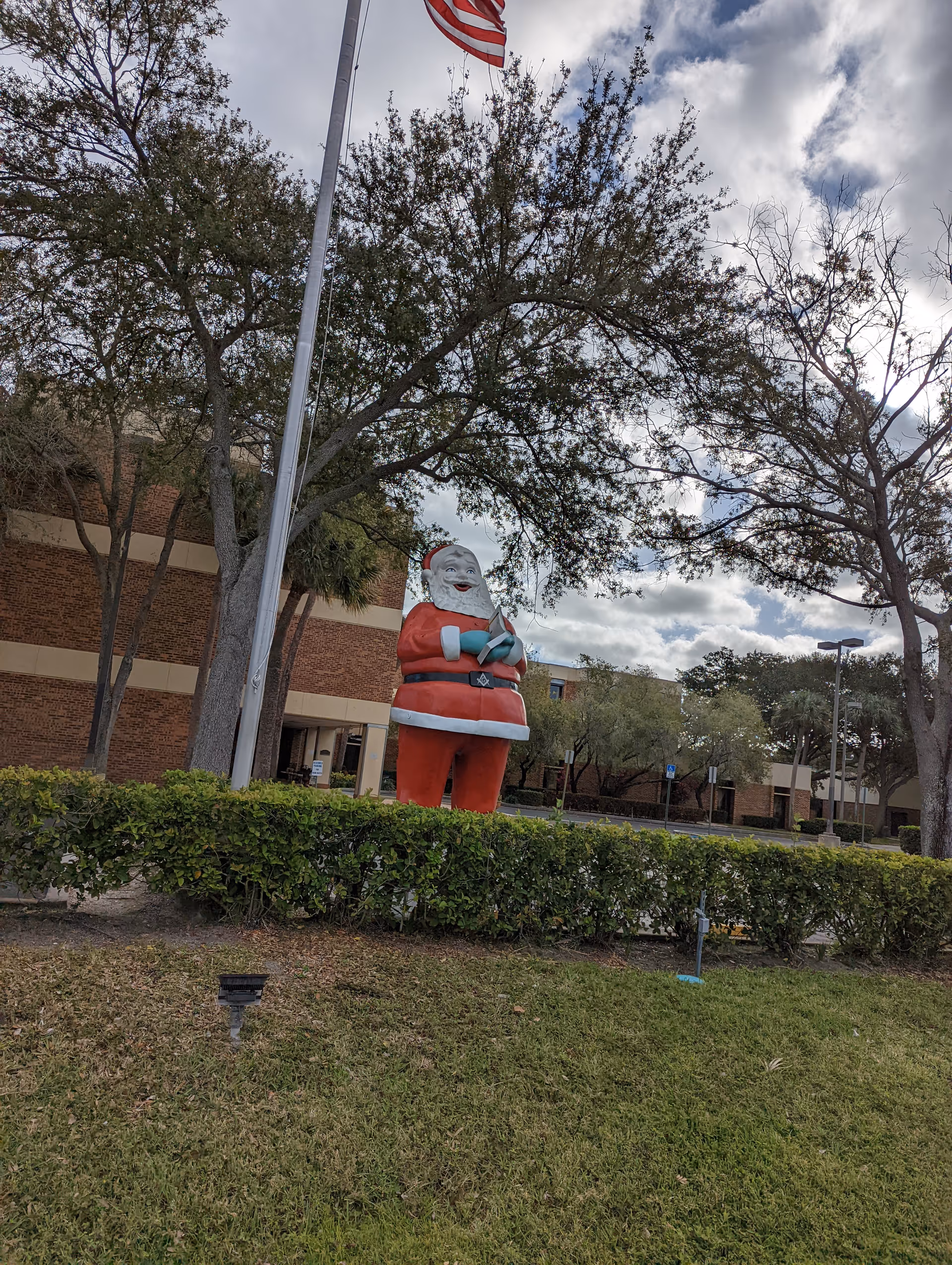Front exterior of Masonic Home with a large Santa statue, flagpole, and trees.