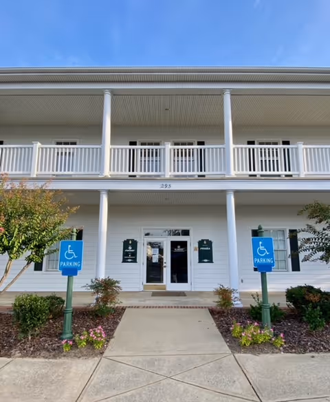Front view of a white senior care facility with wheelchair parking signs.