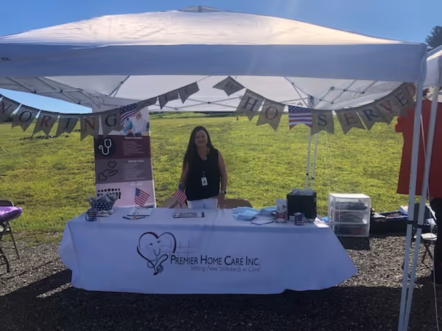A staff member stands at an outdoor information booth for Premier Home Care Inc.