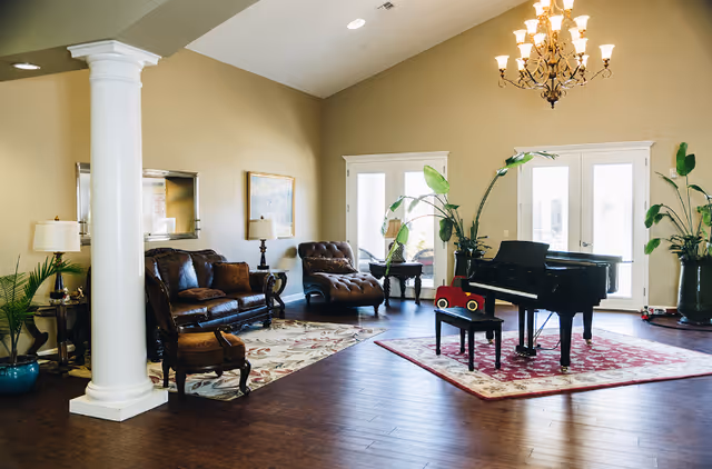 Spacious Grand Manor living room featuring a grand piano, leather seating, and plants.